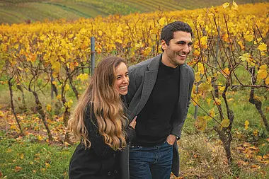 Zwei Personen stehen in einem Weinberg und unterhalten sich bei Sonnenschein.