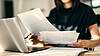 Person sitting at a table with an open laptop and documents.
