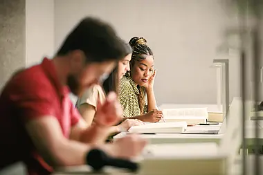 Gruppe von Personen sitzt an einem Tisch und arbeitet gemeinsam mit Dokumenten.